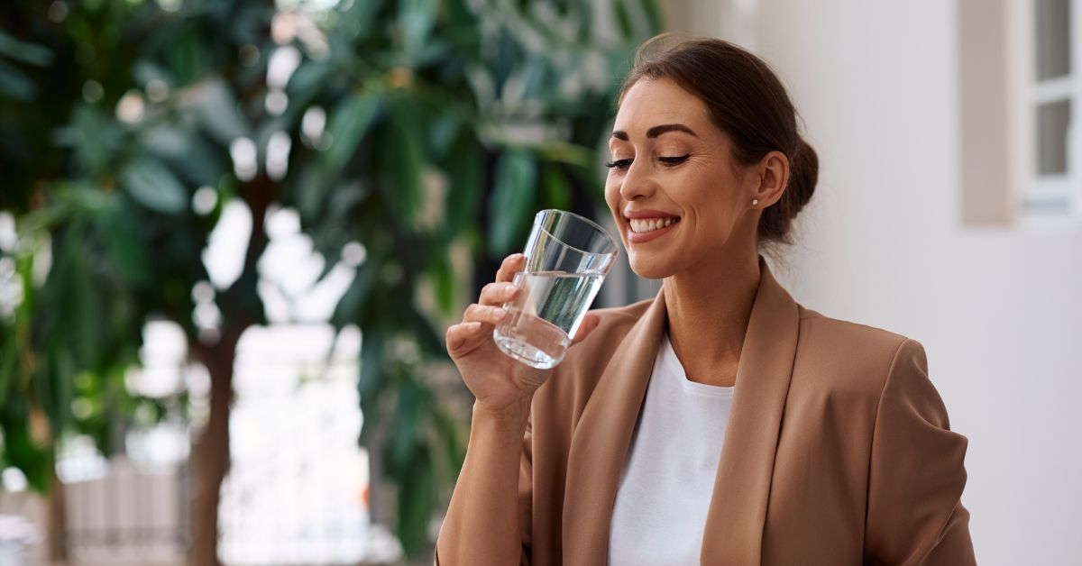Smiling woman enjoying a glass of purified water, illustrating the benefits of a well water conditioner for improved taste.